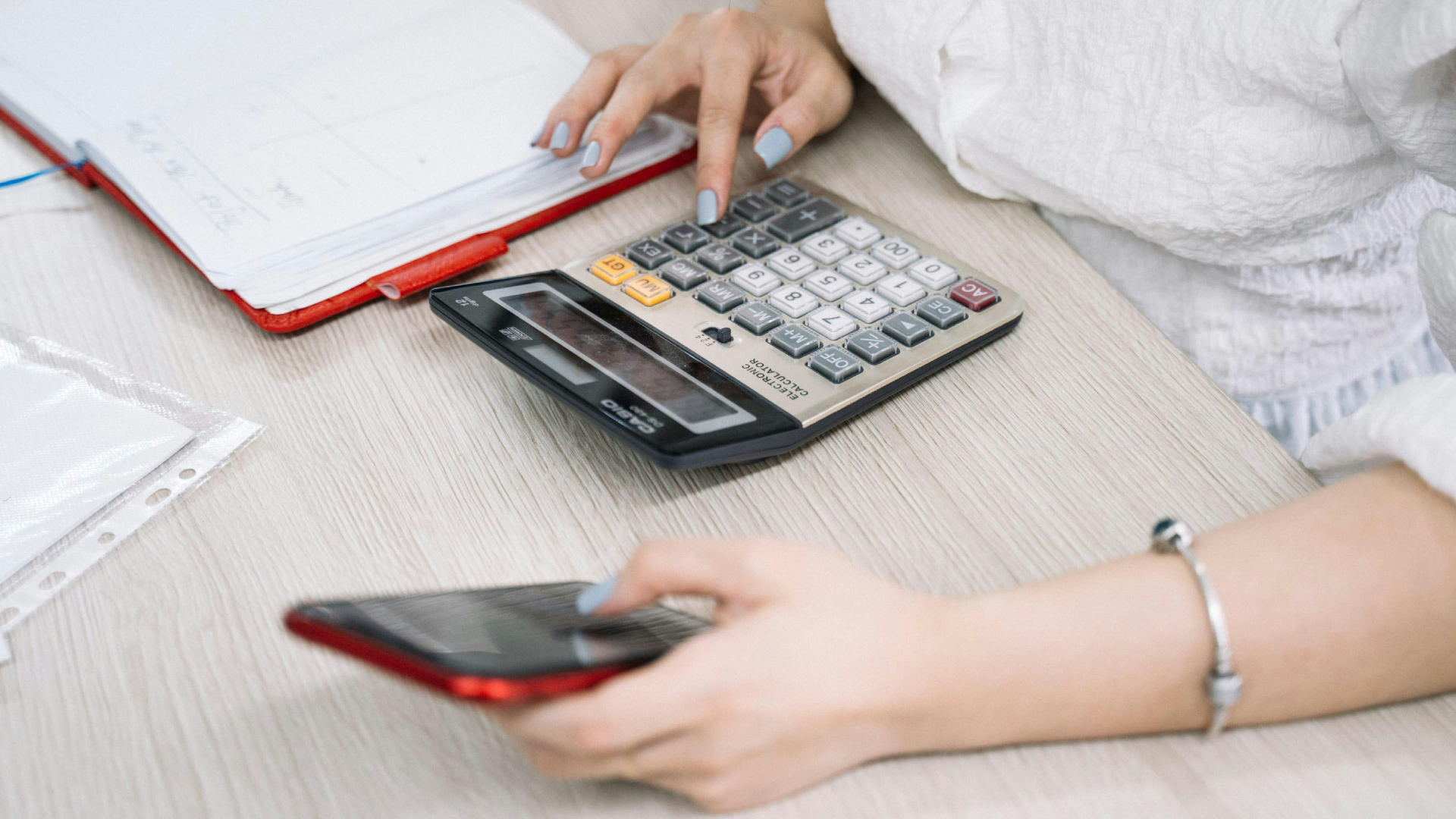 woman's hands punching keys on calculator and holding phone
